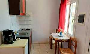 Et lite kjøkken med en vaskebenk og komfyr samt et bord med stoler ved et vindu. (AI-generert tekst)