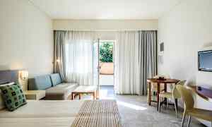 Hotelrom med oppredd seng, sittegruppe, rundt spisebord og balkongdør. (AI-generert tekst)