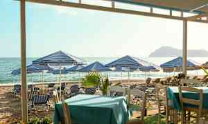 Strand med blå-hvitrutete parasoller og solsenger, bord i forgrunnen. (AI-generert tekst)