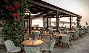 Uteservering med bord og stoler og utsikt mot havet. (AI-generert tekst)