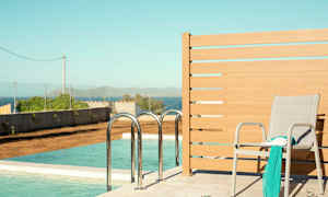 En solstol med et sjal og en bok står ved siden av et basseng med havutsikt. (AI-generert tekst)