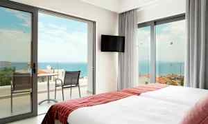 Hotellrom med to senger og dører til en balkong mot havet. (AI-generert tekst)