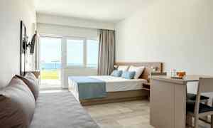 Moderne hotellrom med seng, sofa og spisebord, havutsikt utenfor vinduet. (AI-generert tekst)