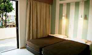 To enkeltsenger i et rom med stripete vegger og en åpen balkongdør som leder til en uteplass. (AI-generert tekst)