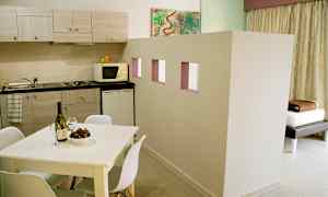 En leilighet med et kjøkken med benkeplate, skap, mikrobølgeovn og kjøleskap. Et hvitt spisebord med stoler står i forgrunnen. (AI-generert tekst)