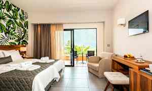 Et hotellrom med dobbeltseng, sittegruppe, balkong og veggdekor med bladmotiv. (AI-generert tekst)