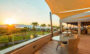 Terrasse med bord og stoler samt utsikt over grøntområde og solnedgang. (AI-generert tekst)