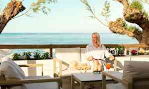 En sittegruppe ved havet med utsikt over blått vann og trær. (AI-generert tekst)