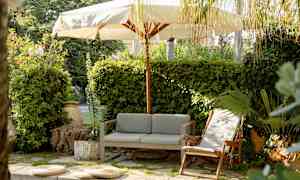 Utendørsområde med sofa, lenestol og parasoll omgitt av grøntområder. (AI-generert tekst)