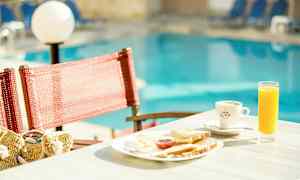 En frokosttallerken med juice og kaffe på et bord ved et basseng. (AI-generert tekst)