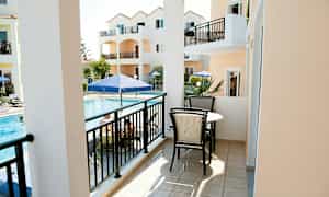 En balkong med møbler, utsikt mot et basseng og oransje bygninger. (AI-generert tekst)