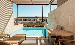 En privat terrasse med solsenger, et bord og basseng, med utsikt mot en bygning i det fjerne. (AI-generert tekst)