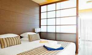 Et hotellrom med en stor seng, trepaneler og en delvis transparent skyvedør. (AI-generert tekst)