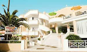 Bygning med hvit fasade og spiraltrapp, omgitt av grøntområder og med skilt som viser 'Rita Suites'. (AI-generert tekst)