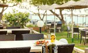 Et bord med en tallerken salat og et glass øl på en terrasse med utemøbler og strandparasoller i bakgrunnen. (AI-generert tekst)