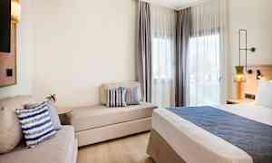 Moderne hotellrom med seng, sofa og vinduer med lyse gardiner. (AI-generert tekst)