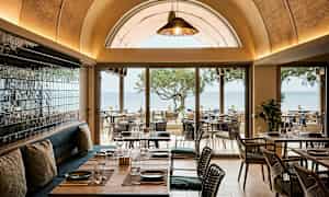 Restaurant med utsikt over havet, møbler i tre og glassdetaljer. (AI-generert tekst)