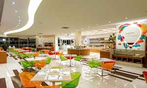 En spisesal med fargerike stoler og dekkede bord, samt en buffet i bakgrunnen. (AI-generert tekst)