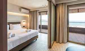 Hotellrom med seng og håndklær, store glassdører som fører ut til en balkong med havutsikt. (AI-generert tekst)