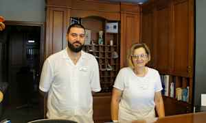 To personer står ved en resepsjonsdisk med trepaneler i bakgrunnen. (AI-generert tekst)