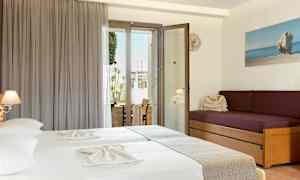 Et hotellrom med to senger med lyse laken, en lilla sofa med puter, og en glassdør som fører ut til en balkong. (AI-generert tekst)