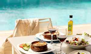 Tallerkener med greske retter, to glass rødvin og et basseng i bakgrunnen. (AI-generert tekst)