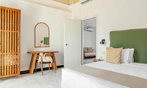 Et soverom med en grønn sengegavl, et trebord med et speil over og et garderobeskap med trepanel. (AI-generert tekst)