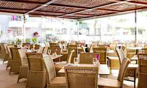 Restaurant med rottingmøbler og blomster på bordene. (AI-generert tekst)