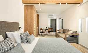 Hotellrom med en dobbeltseng i forgrunnen, treinteriør og et lite sitteområde med bord og to stoler i bakgrunnen. (AI-generert tekst)