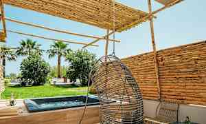 Bilde av en terrasse med boblebad, hengestol og tremøbler, omgitt av trær og busker. (AI-generert tekst)