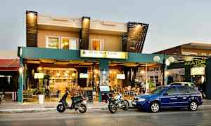 Fasaden til Akatos Hotel med biler og motorsykler parkert foran. (AI-generert tekst)