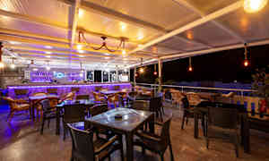 En utendørs bar med stoler og bord, opplyst med varm belysning om natten. (AI-generert tekst)