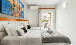 Dobbeltrom med hvite vegger, en dobbeltseng med grå sengeteppe og et bilde av seilbåter på veggen. (AI-generert tekst)