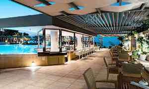 Restaurant vendt mot et basseng og utendørsområde med havutsikt om kvelden. (AI-generert tekst)