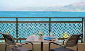 To stoler ved et bord med en karaffel og to glass, med utsikt over havet. (AI-generert tekst)