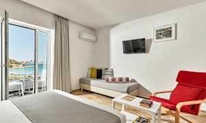 Et hotellrom med sittegruppe, seng og utsikt mot en strand gjennom en glassdør. (AI-generert tekst)