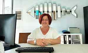 Person sitter ved et skrivebord med tastatur, dataskjerm og hyller i bakgrunnen. (AI-generert tekst)