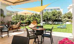 En terrasse med bord, stoler og hengesofaer, omgitt av en plen med solsenger og trær. (AI-generert tekst)