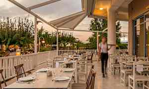 Uteservering med dekkede bord under tak, omgitt av grøntområder. (AI-generert tekst)