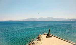 En steinete strand og hav med et kunstverk synlig på en brygge. (AI-generert tekst)