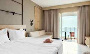 Hotellrom med seng, sofa og balkong med havutsikt. (AI-generert tekst)