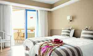 Et hotellrom med to enkeltsenger, stripete sengetøy og en dør til en balkong. (AI-generert tekst)