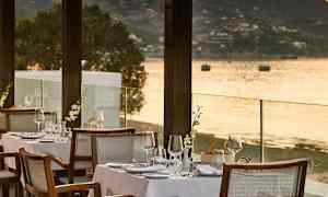 En uteservering med dekkede bord ved vannkanten og utsikt over sjøen. (AI-generert tekst)