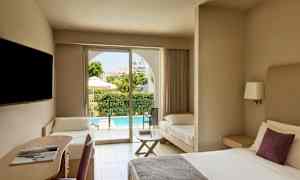 Et hotellrom med en dobbeltseng, en skriveplass og en ekstra seng. Utenfor vises en terrasse og et basseng. (AI-generert tekst)