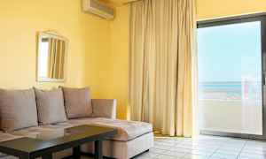 En stue med beige hjørnesofa, glassbord, speil på veggen og stor vindusdør med gardiner og utsikt. (AI-generert tekst)