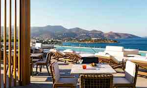 En terrasse med utsikt over havet og fjell i bakgrunnen, med solsenger og bord. (AI-generert tekst)