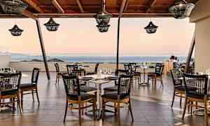 En restaurant med bord og stoler på en terrasse med utsikt over havet. (AI-generert tekst)