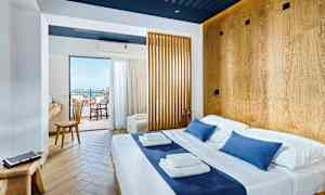 Lyst hotellrom med dobbeltseng og tredetaljer, utsikt mot balkong og hav. (AI-generert tekst)