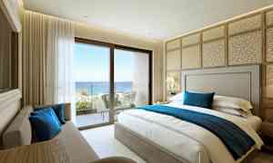 Et hotellrom med en dobbeltseng, sofa og utsikt mot havet fra en balkong. (AI-generert tekst)