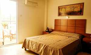 Et soverom med en seng, et nattbord og et maleri på veggen; ved siden av er en åpen balkongdør. (AI-generert tekst)